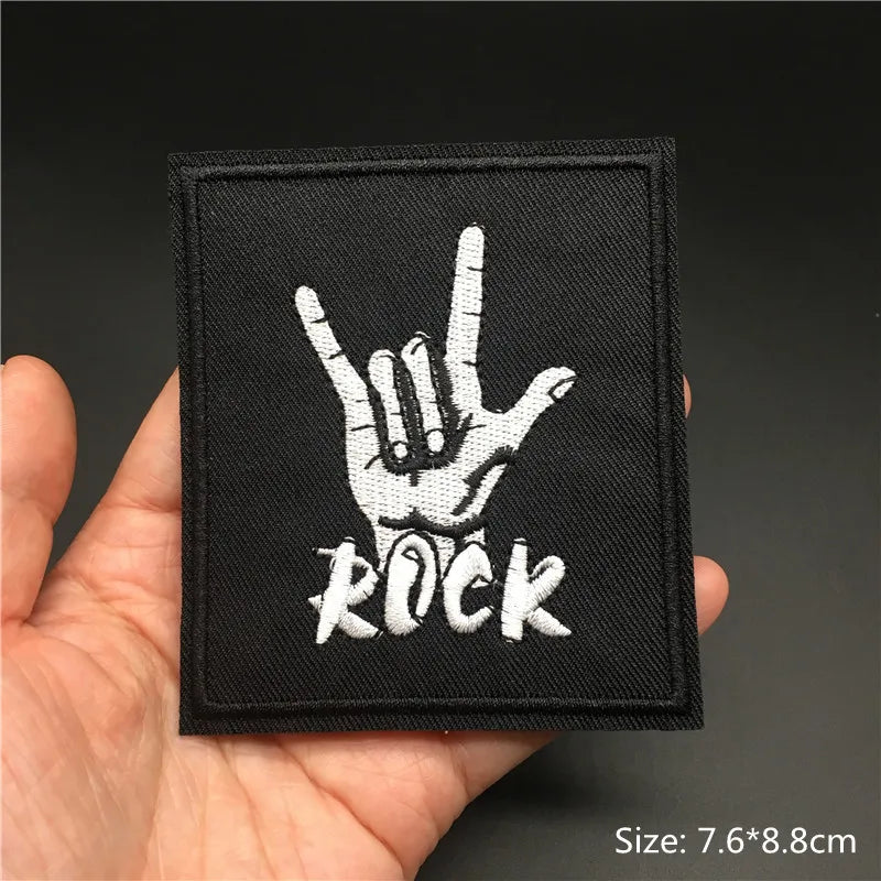 Black patch with white hand gesture and 'ROCK' text held in a hand against a dark background