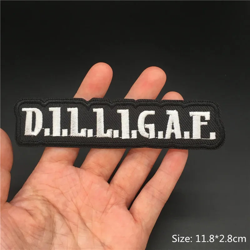 Hand holding a black and white D.I.L.L.I.G.A.F. embroidered iron-on patch approx 11.8x2.8cm on a dark background