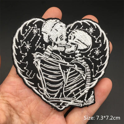 Heart-shaped patch with skeletons holding hands on a hand, against a dark background.