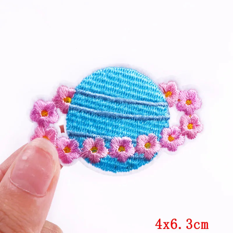 Blue circular hair clip with pink flowers held by a hand on a white background