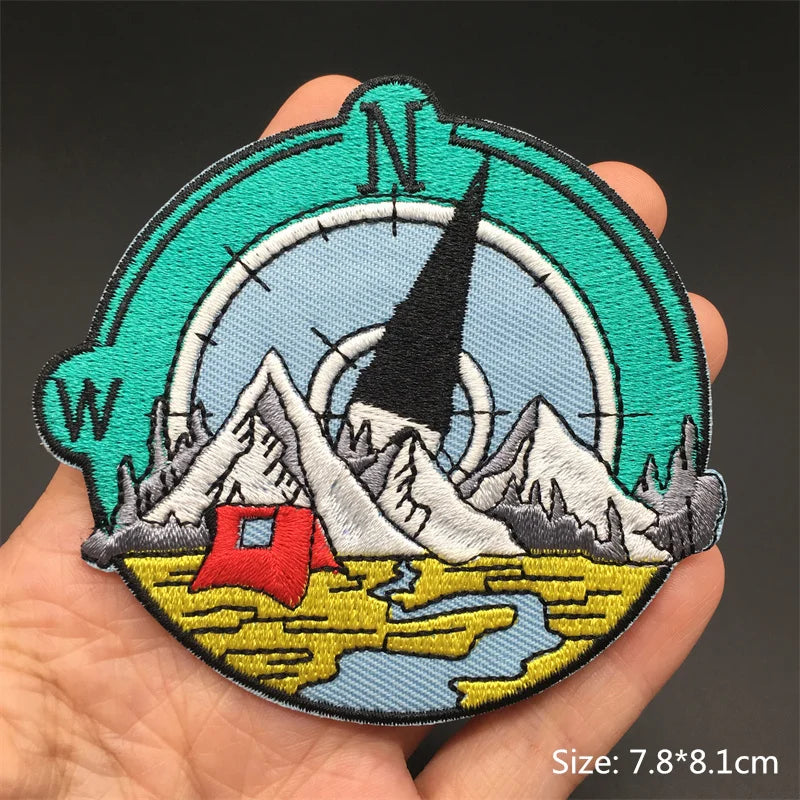 Embroidered patch with mountain and cabin design held in a hand