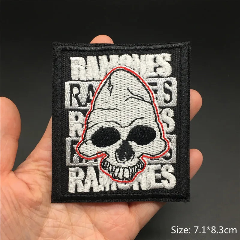 Embroidered patch with skull design and text held in a hand against a dark background