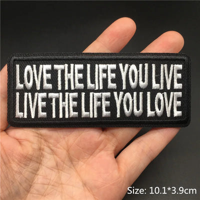 Embroidered patch with 'Love the life you live, live the life you love' text held in a hand.