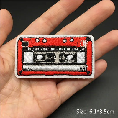 Embroidered patch of a cassette tape held in a hand with a dark background