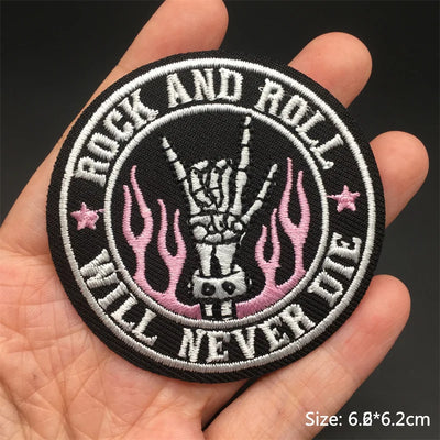 Circular patch with 'Rock and Roll Will Never Die' text and skeleton hand design held in a hand.