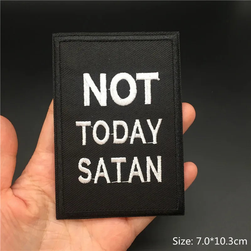 Black patch with 'Not Today Satan' text held in a hand against a dark background