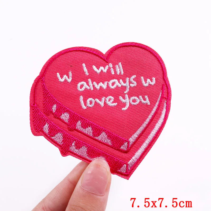 Heart-shaped pink patch with 'I will always love you' text held by a hand on a white background