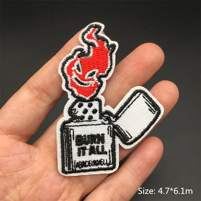Embroidered patch of a lighter with flames held in a hand against a dark background