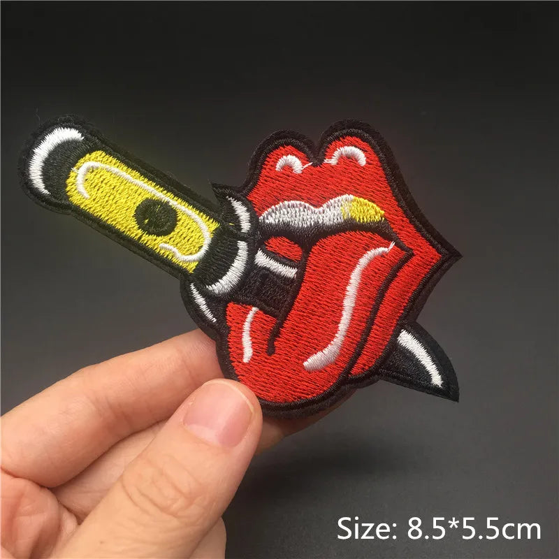 Embroidered patch of a tongue and knife design held by a hand on a dark background
