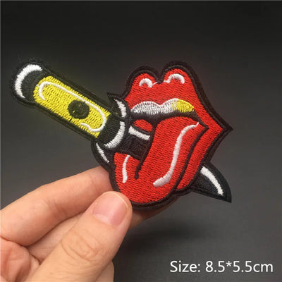 Embroidered patch of a tongue and knife design held by a hand on a dark background