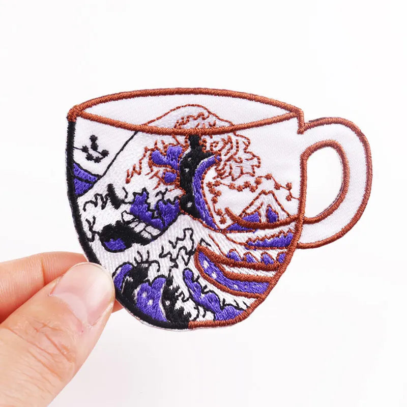 Embroidered patch of a teacup with dragon design held by a hand on a white background