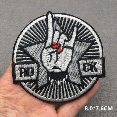 Embroidered patch with a hand gesture held by a person's hand on a gray background