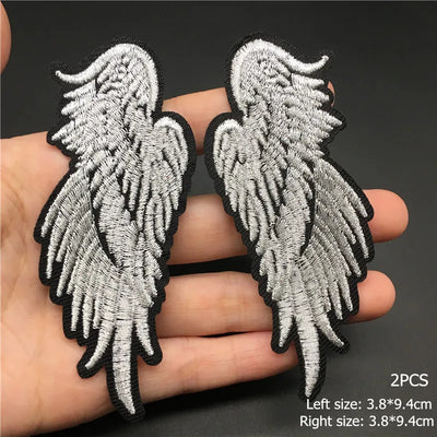 Two silver angel wing patches held between fingers with size information on a dark background.