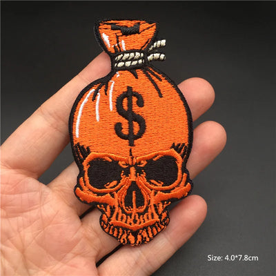 Patch of a skull with a money bag and dollar sign held in a hand against a dark background.