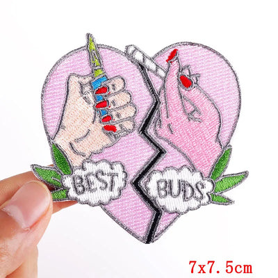 Heart-shaped patch with two hands holding a sword and shield, labeled 'Best Buds', held by a hand.