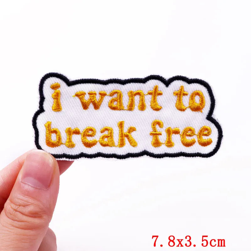 Embroidered patch with 'i want to break free' text held by a hand on a white background