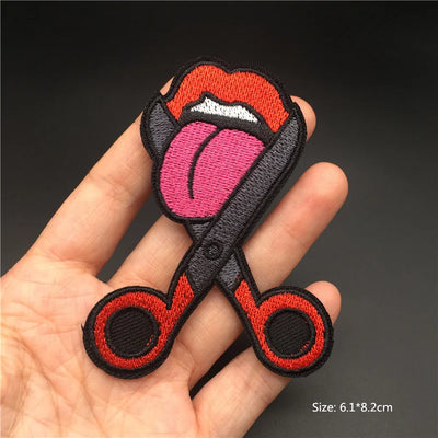 Embroidered patch of a tongue and scissors held in a hand with a dark background