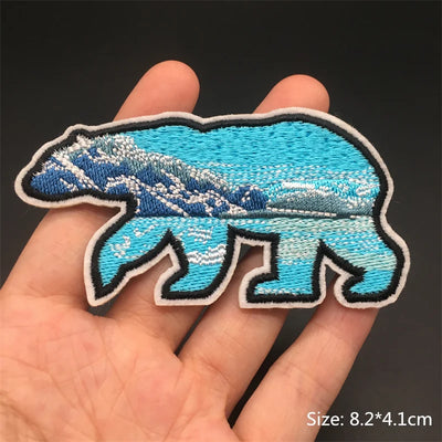 Blue bear-shaped patch held in a hand with a dark background