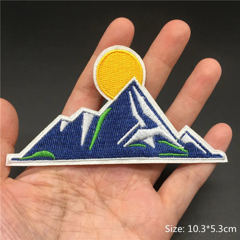 Embroidered patch of mountains and sun held in a hand with a dark background