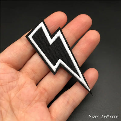 Black and white lightning bolt patch held in a hand with a dark background