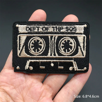 Embroidered patch of a cassette tape held in a hand with a dark background