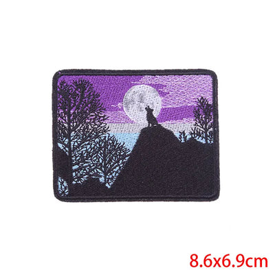 Embroidered patch of a wolf howling at the moon with trees, on a white background.