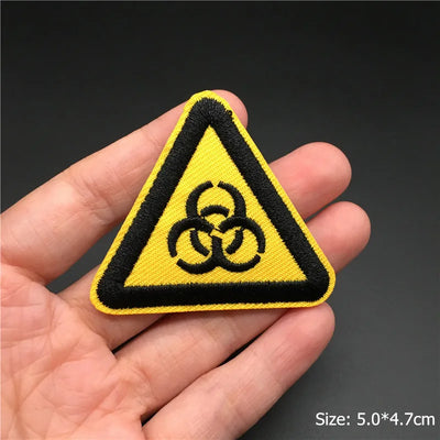 Yellow triangle biohazard warning patch held in a hand with a dark background
