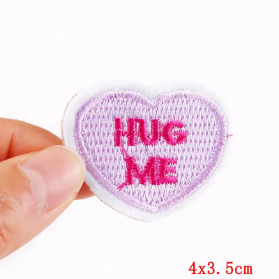 Heart-shaped patch with 'Hug Me' text held by a hand on a white background