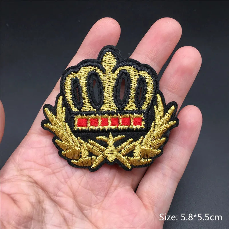 Embroidered patch with a crown design held in a hand against a dark background