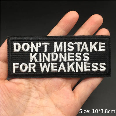 Embroidered patch with 'Don't mistake kindness for weakness' text held in a hand against a dark background.