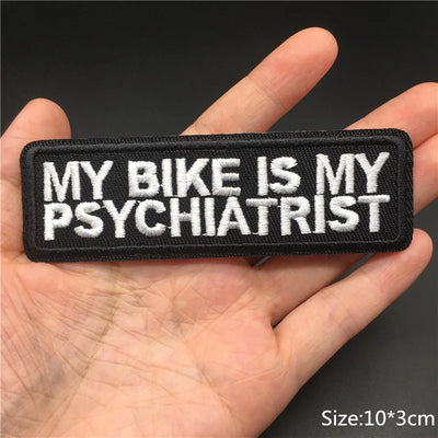 Embroidered patch with 'My bike is my psychiatrist' text held in a hand against a dark background.
