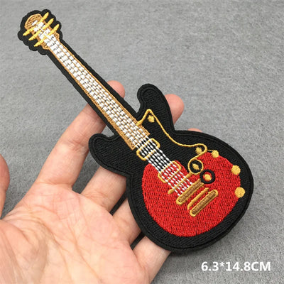 Embroidered patch of a guitar held by a hand on a gray background