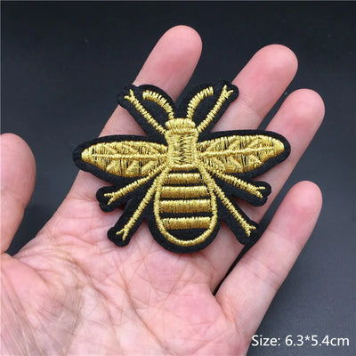 Gold and black bee patch held in a hand with a dark background
