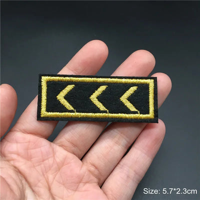 Yellow arrow patch on a black background held in a hand with a dark background