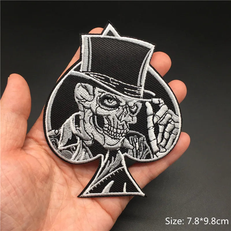 Embroidered patch of a skeleton in a top hat held in a hand against a dark background