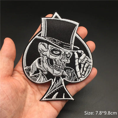 Embroidered patch of a skeleton in a top hat held in a hand against a dark background