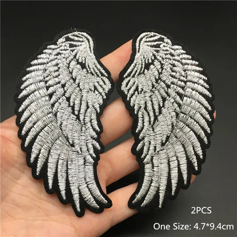 Pair of silver angel wings patches held by a hand on a dark background