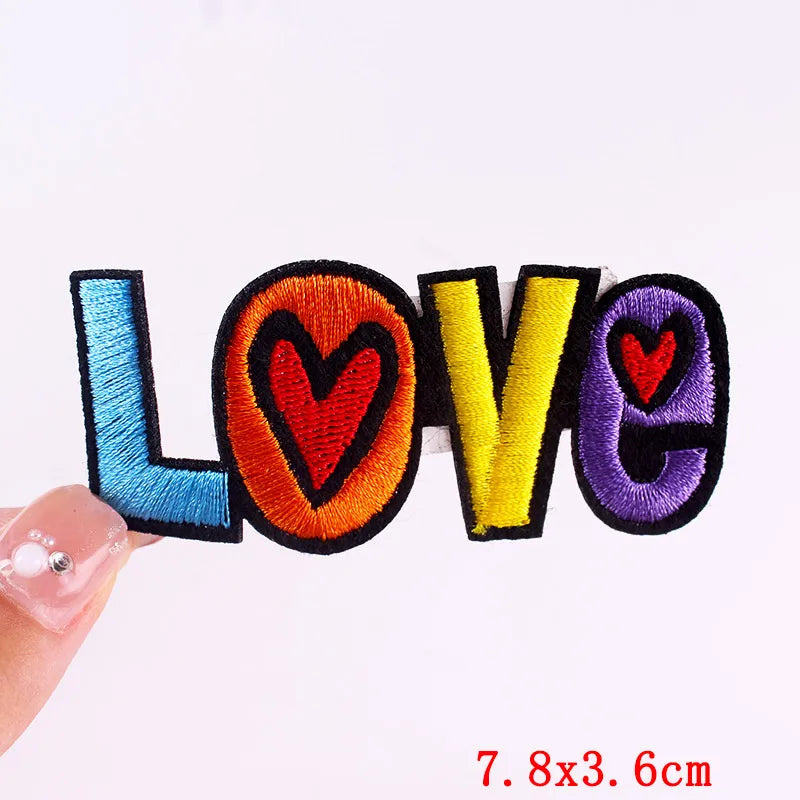 Colorful 'LOVE' patch held by a hand with measurement text on a white background