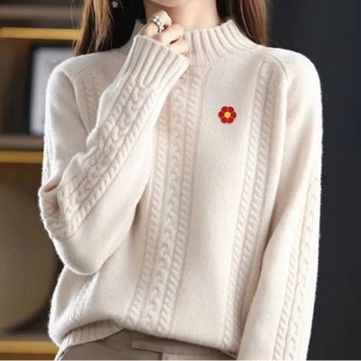 Person wearing a beige cable knit sweater with a red flower brooch.