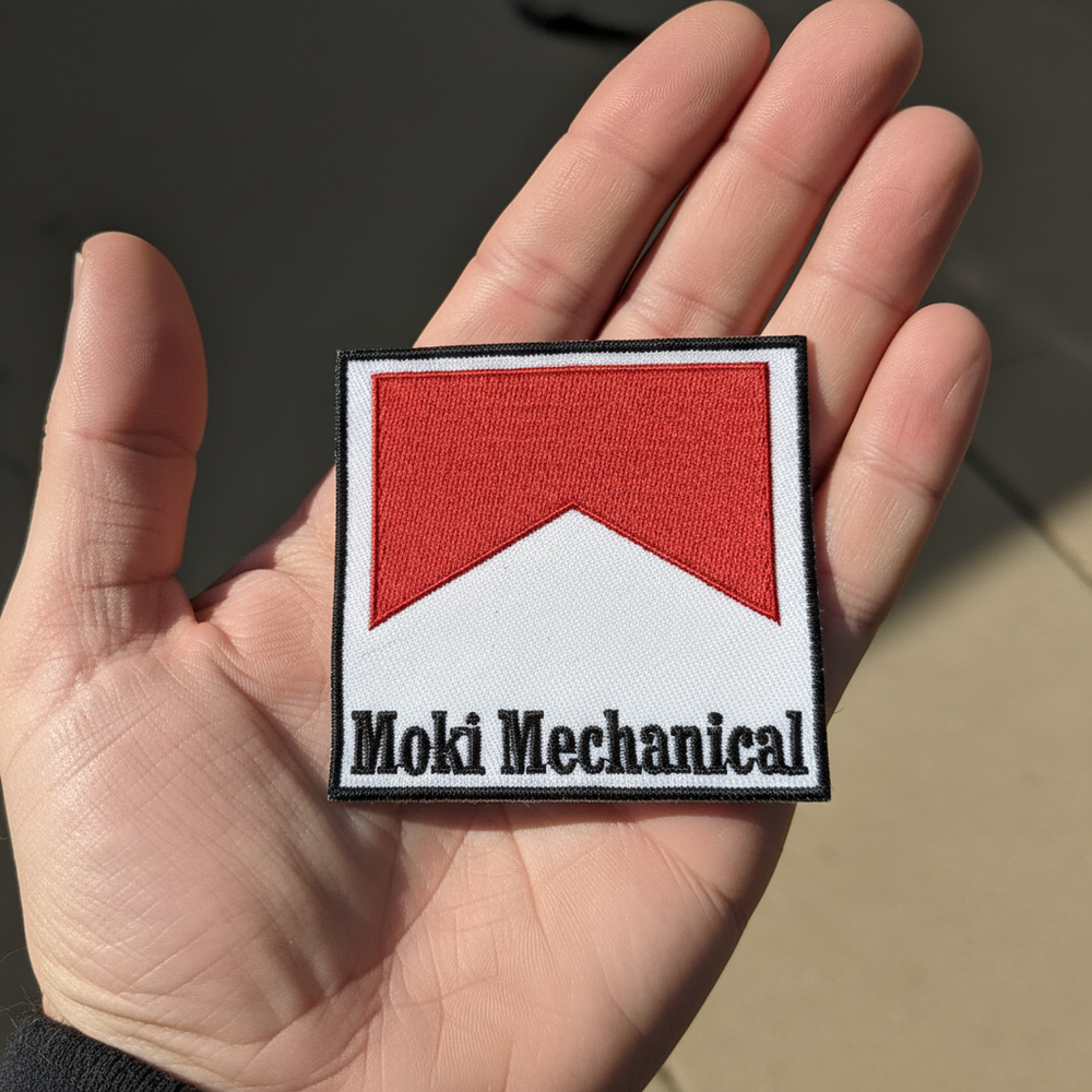 Patch with red and white design and 'Moki Mechanical' text held on hand 