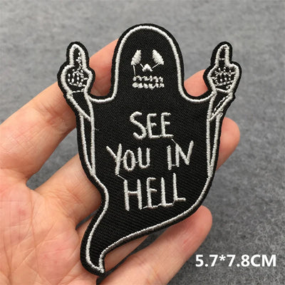 Ghost-shaped patch with 'See You in Hell' text held in a hand against a gray background