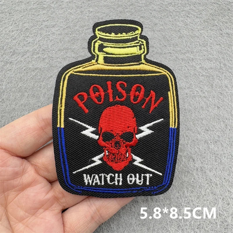 Embroidered patch of a poison bottle with skull design held in hand on gray background