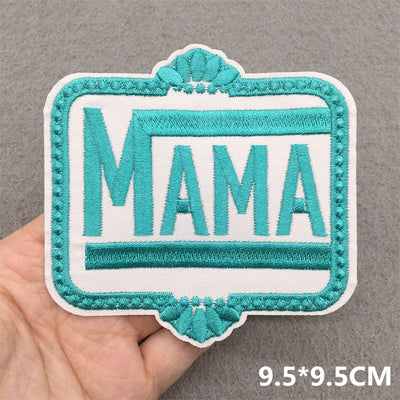 Embroidered patch with 'MAMA' text held by a hand on a gray background
