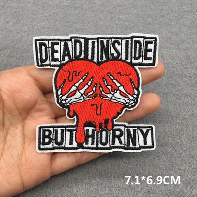 Embroidered patch with skeleton hands holding a heart and text held in a hand against a gray background