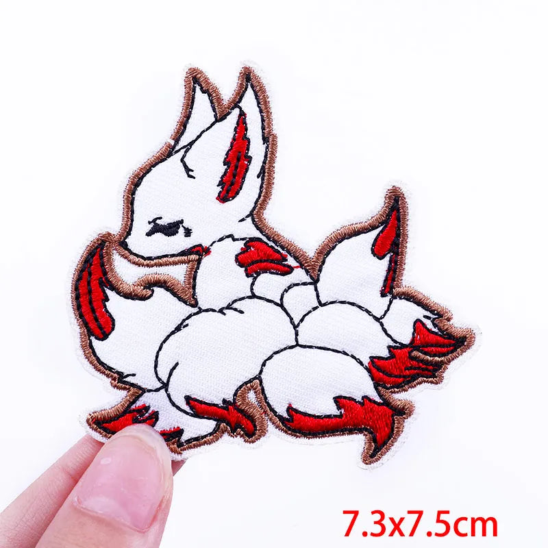 Embroidered patch of a white rabbit with red accents held by a hand, on a white background.