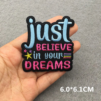 Embroidered patch with 'Just Believe in Your Dreams' text held in a hand on a gray background