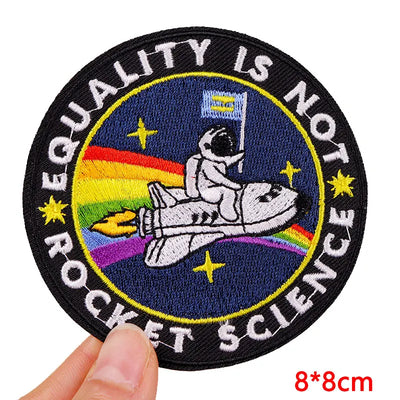 Patch with astronaut, rainbow, and text 'Equality is not rocket science' held by a hand.