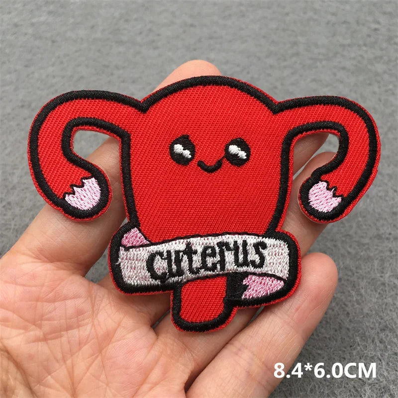 Red uterus-shaped patch with a smiling face held in a hand on a gray background