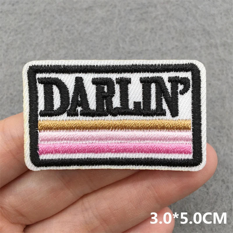 Embroidered patch with 'DARLIN'' text held in a hand against a gray background