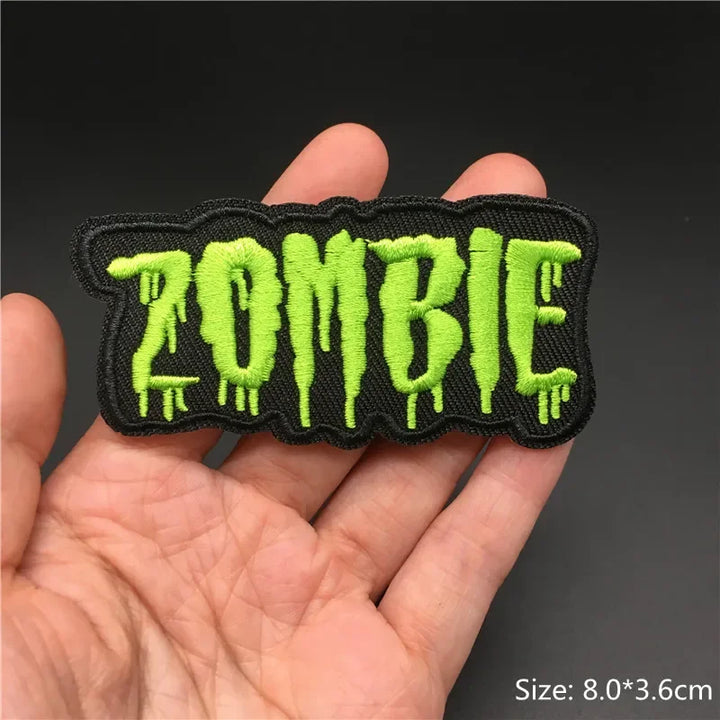 Hand holding a black and neon green Zombie embroidered iron-on patch 8x3.6cm on a dark background